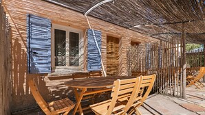 Une table et des chaises en bois sont placées à l’extérieur d’un bâtiment dont la façade est en briques et les volets bleus.