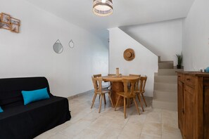 Un salon avec un canapé noir, une table à manger en bois et des chaises, un escalier et un coin cuisine avec des placards.