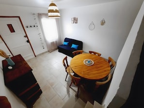 Zona pranzo con tavolo e sedie in legno, un divano e una lampada a sospensione.