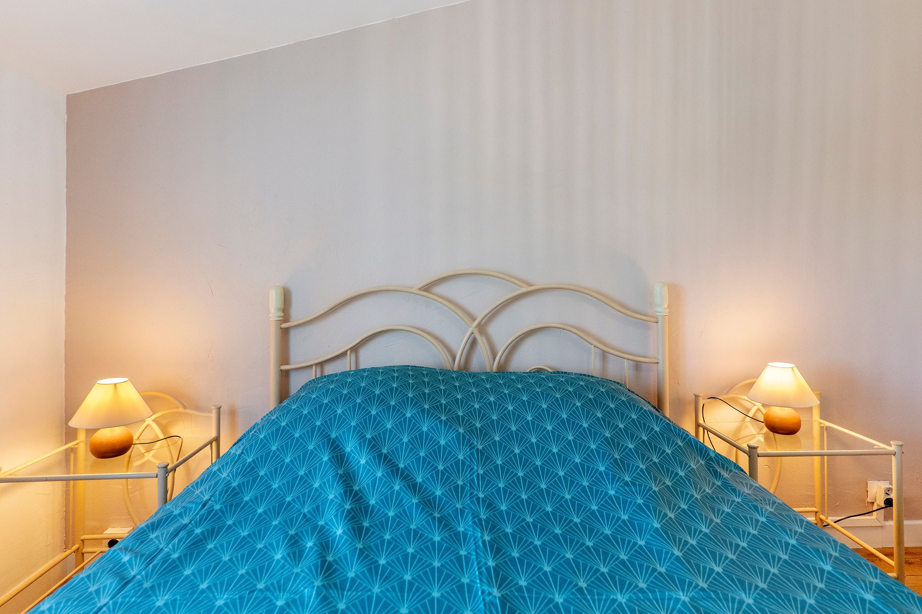 A bed with a geometric patterned bedspread, two bedside lamps, and a metal headboard.
