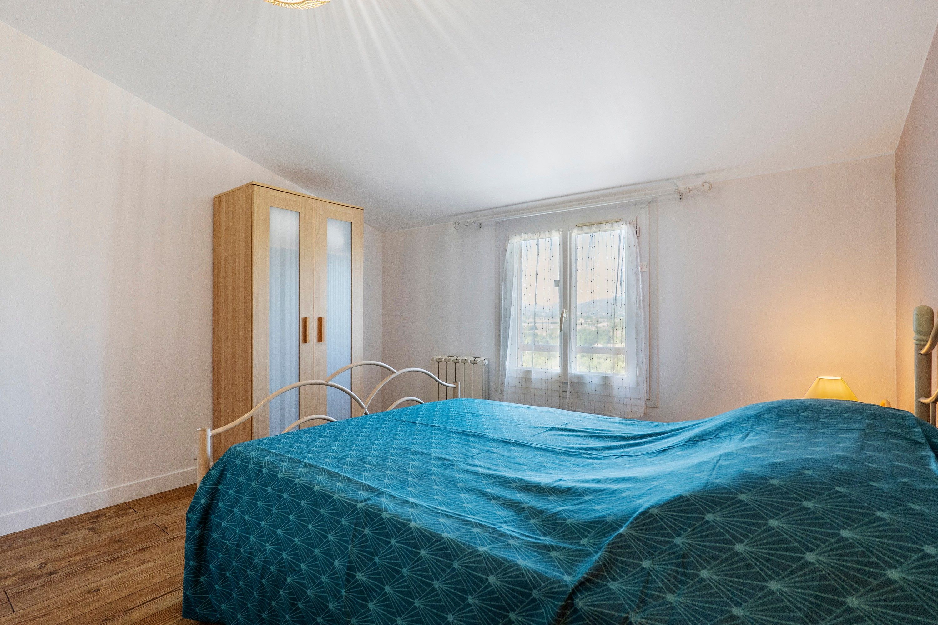 A bedroom with a bed, a wardrobe, a window with curtains, and a radiator.