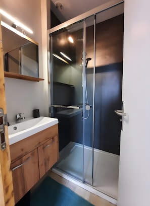 A modern bathroom with a glass-enclosed shower, a white sink, and wooden cabinets.