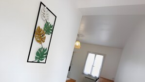 Un pasillo estrecho con un comedor que incluye una mesa y sillas, una ventana con persianas y una obra de arte colgada en la pared con motivos de hojas.