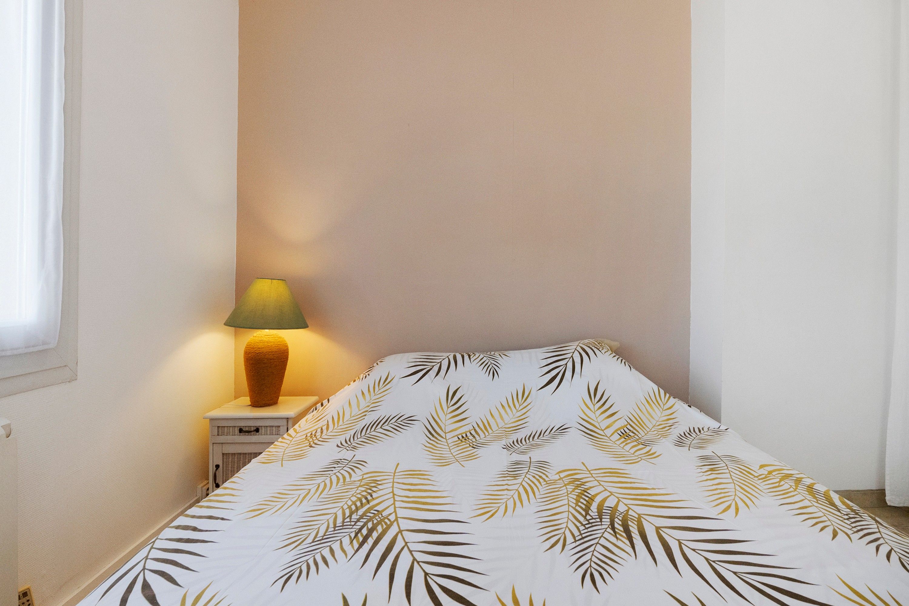 Une chambre à coucher avec un lit, une table de chevet, une lampe et une fenêtre.
