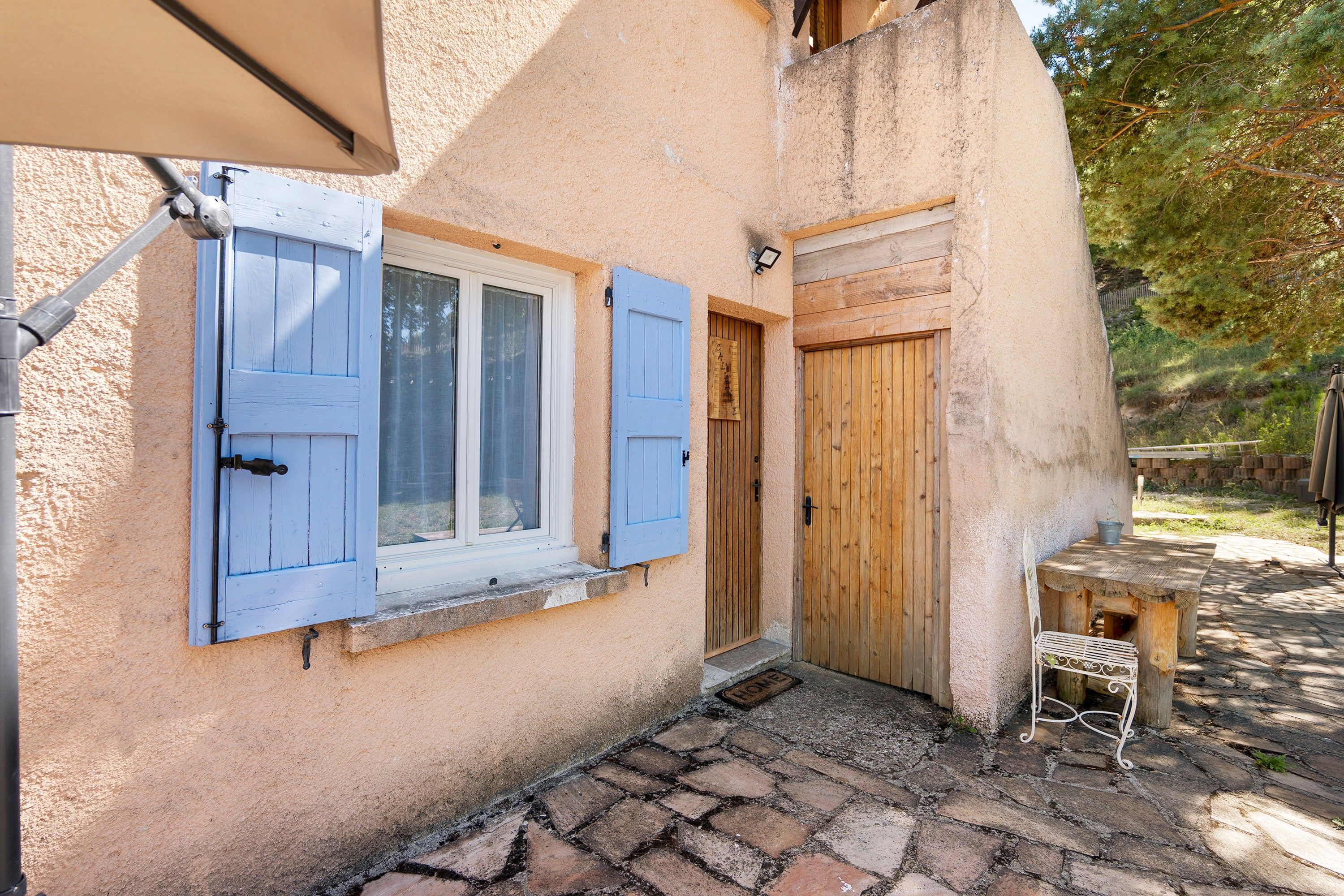 Un edificio rústico con un patio empedrado de piedra, contraventanas de madera en las ventanas y una puerta de madera.