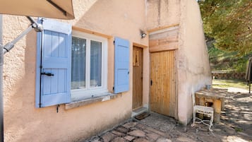 Un edificio rústico con un patio empedrado de piedra, contraventanas de madera en las ventanas y una puerta de madera.