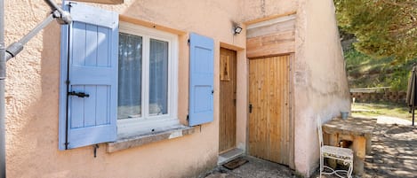 A rustic building with a stone-paved courtyard, wooden shutters on the windows, and a wooden door.