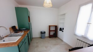 Cocina compacta con lavamanos, armarios verdes, una mesa de madera, un cubo de basura y un estante con electrodomésticos.