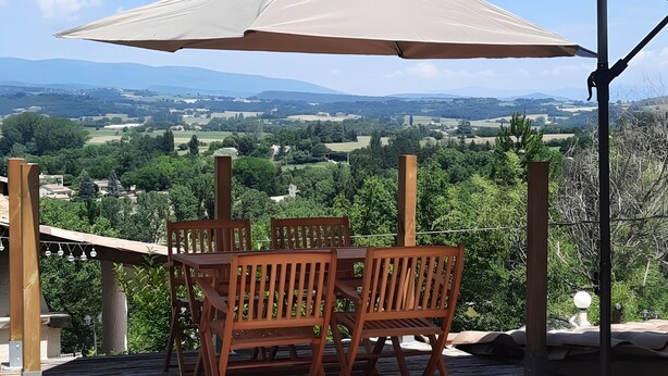 Un patio con mesa y sillas bajo una pérgola, con vistas a un paisaje pintoresco.