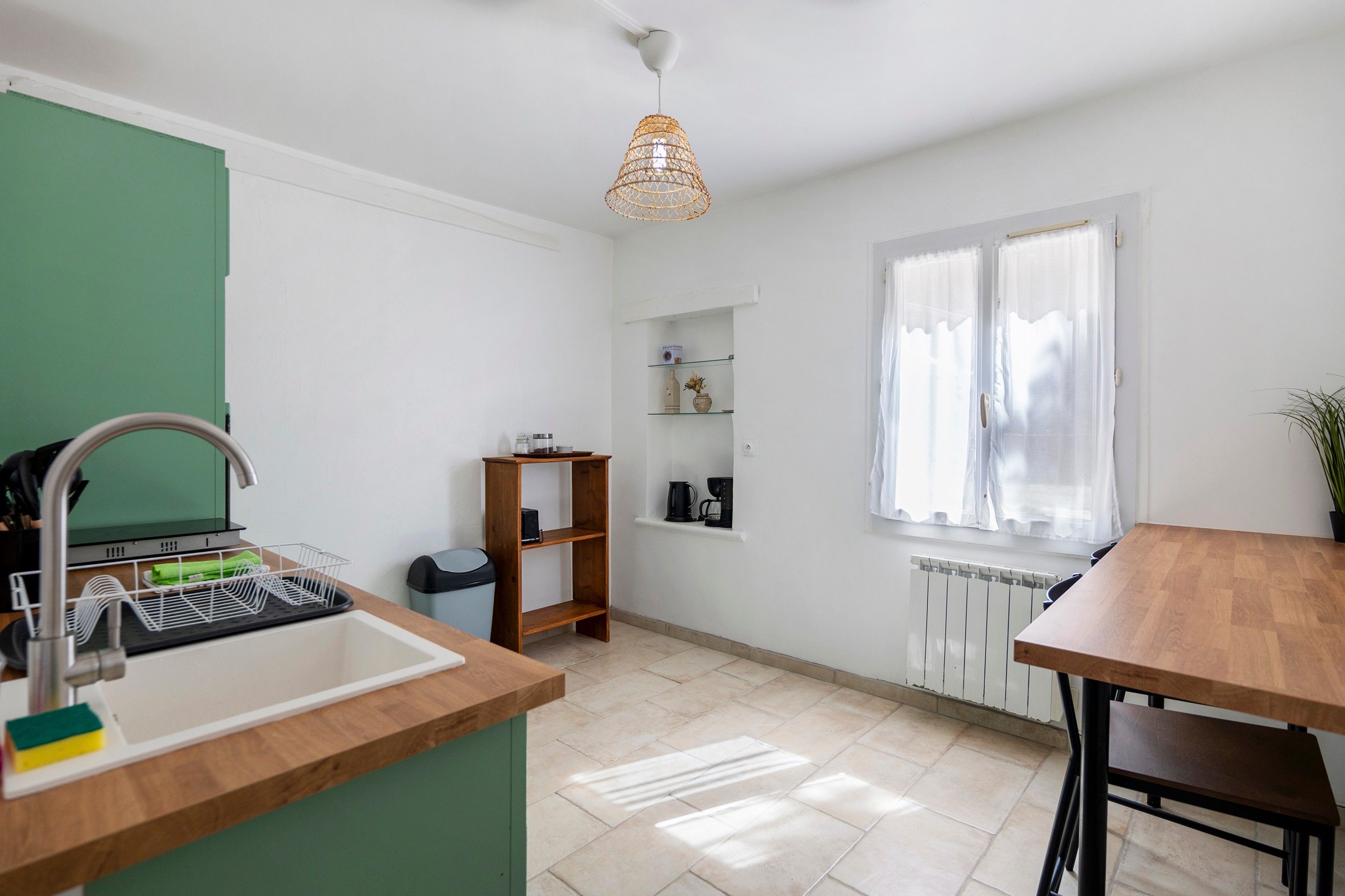 Une cuisine avec un évier, une étagère en bois, une fenêtre et une table.