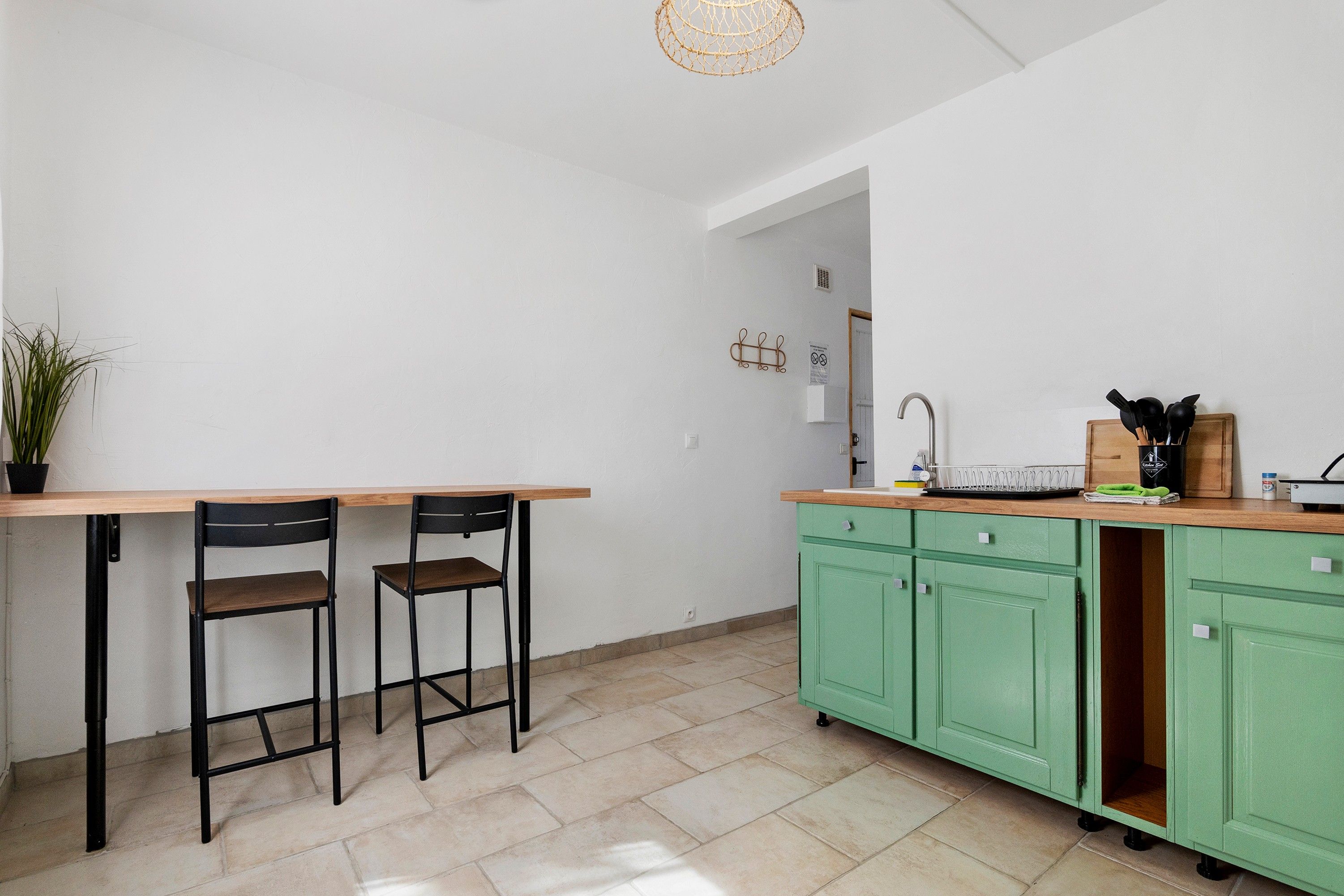 Una cocina con mesa de madera y dos sillas, un lavamanos y armarios verdes.