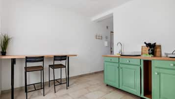 Una cocina con mesa de madera y dos sillas, un lavamanos y armarios verdes.