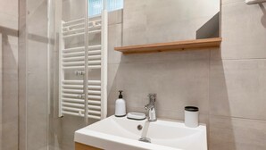 Une salle de bain avec un lavabo blanc, un miroir, une étagère en bois et une cabine de douche en verre.