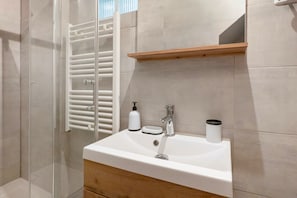 Een badkamer met een witte wasbak, een spiegel, een houten plank en een douchecabine van glas.