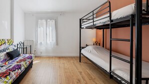 Une pièce avec un lit superposé, un canapé agrémenté de coussins colorés, une fenêtre avec des rideaux et un plancher en bois.