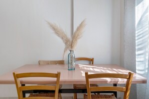 Une table à manger ornée d’un vase rempli de plumes d’herbe des pampas, de deux chaises en bois et d’une nappe de couleur claire.