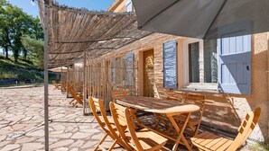 Un espace extérieur aménagé avec des tables et des chaises en bois, un toit de chaume et un sol pavé de pierres.