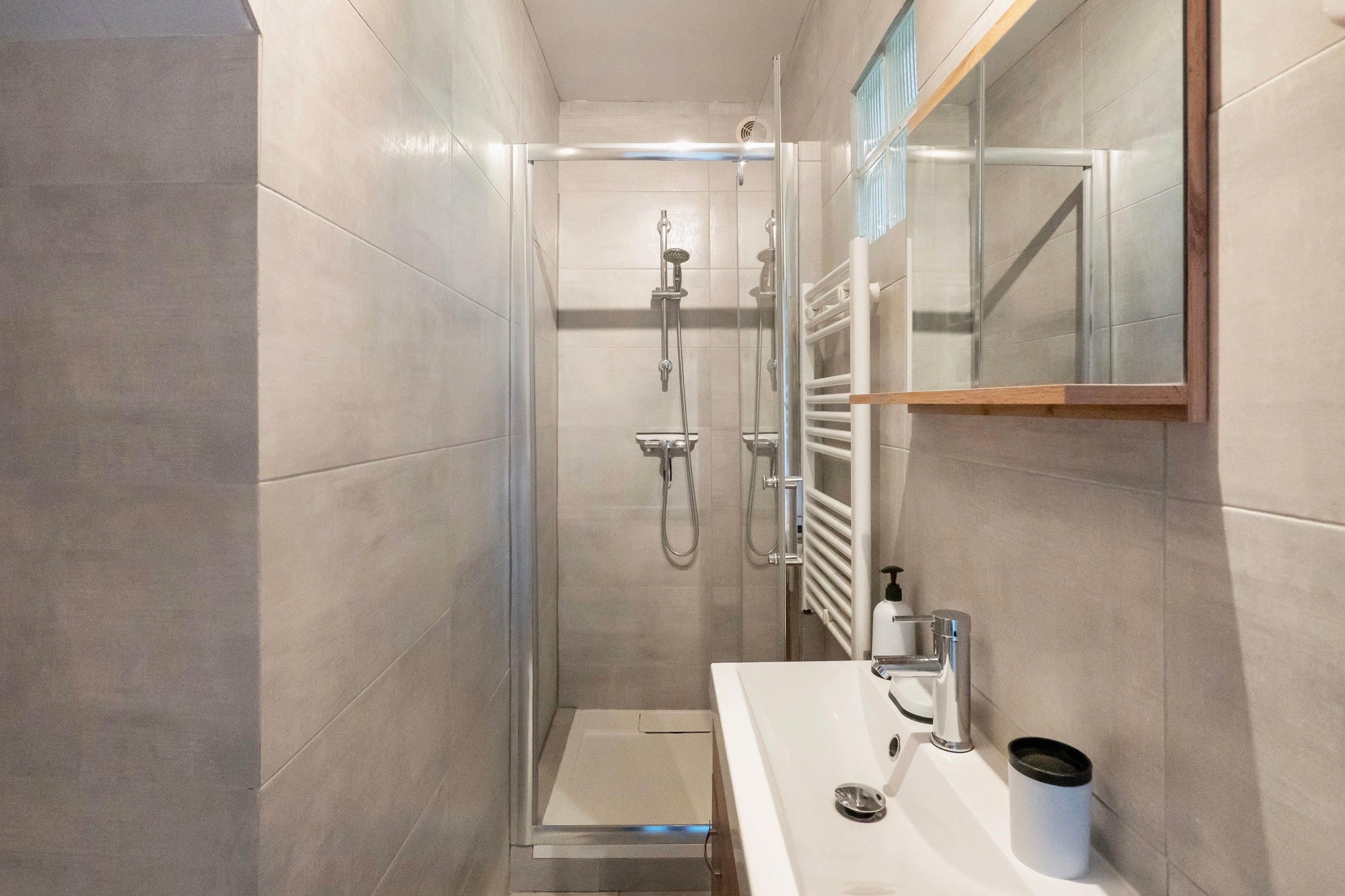 Une salle de bain moderne avec une douche à parois de verre, un lavabo blanc et un miroir au-dessus du lavabo.