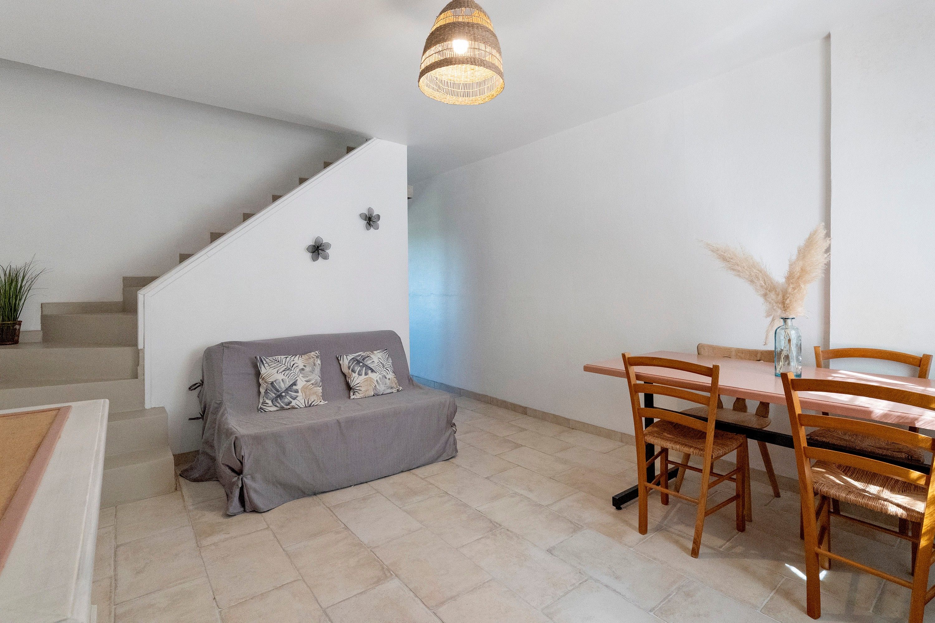 Um interior moderno com escada, um sofá com almofadas estampadas, uma mesa de jantar com cadeiras e um lustre.