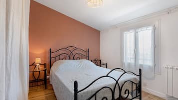 Ein Schlafzimmer mit einem Bett, einem Nachttisch, einer Lampe, einem Fenster mit Vorhängen und einer Heizung.