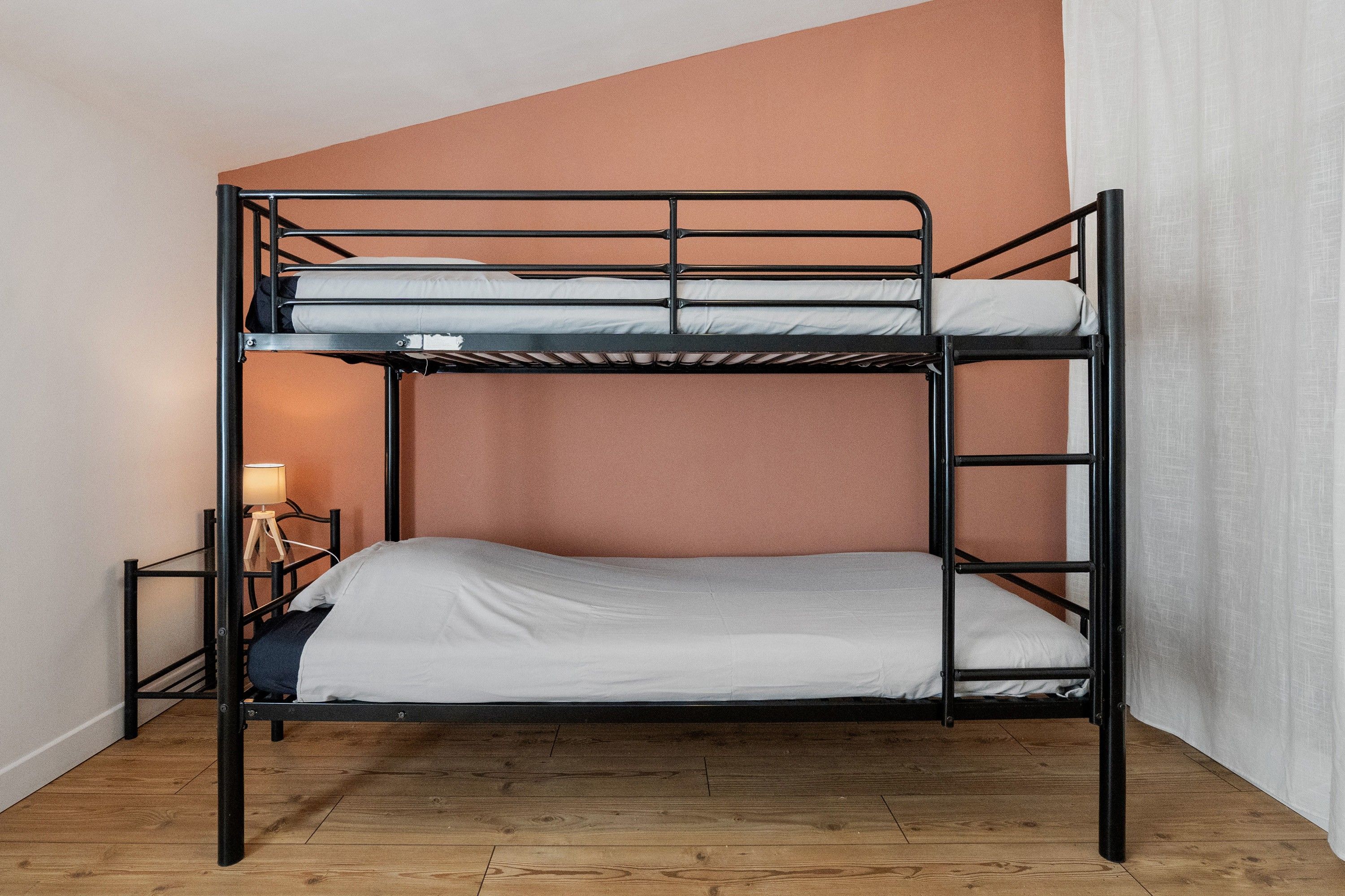 A bunk bed with a wooden floor and a lamp on a side table.