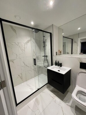 Une salle de bain moderne avec une douche à parois de verre, un lavabo blanc, un meuble-lavabo noir et des toilettes.