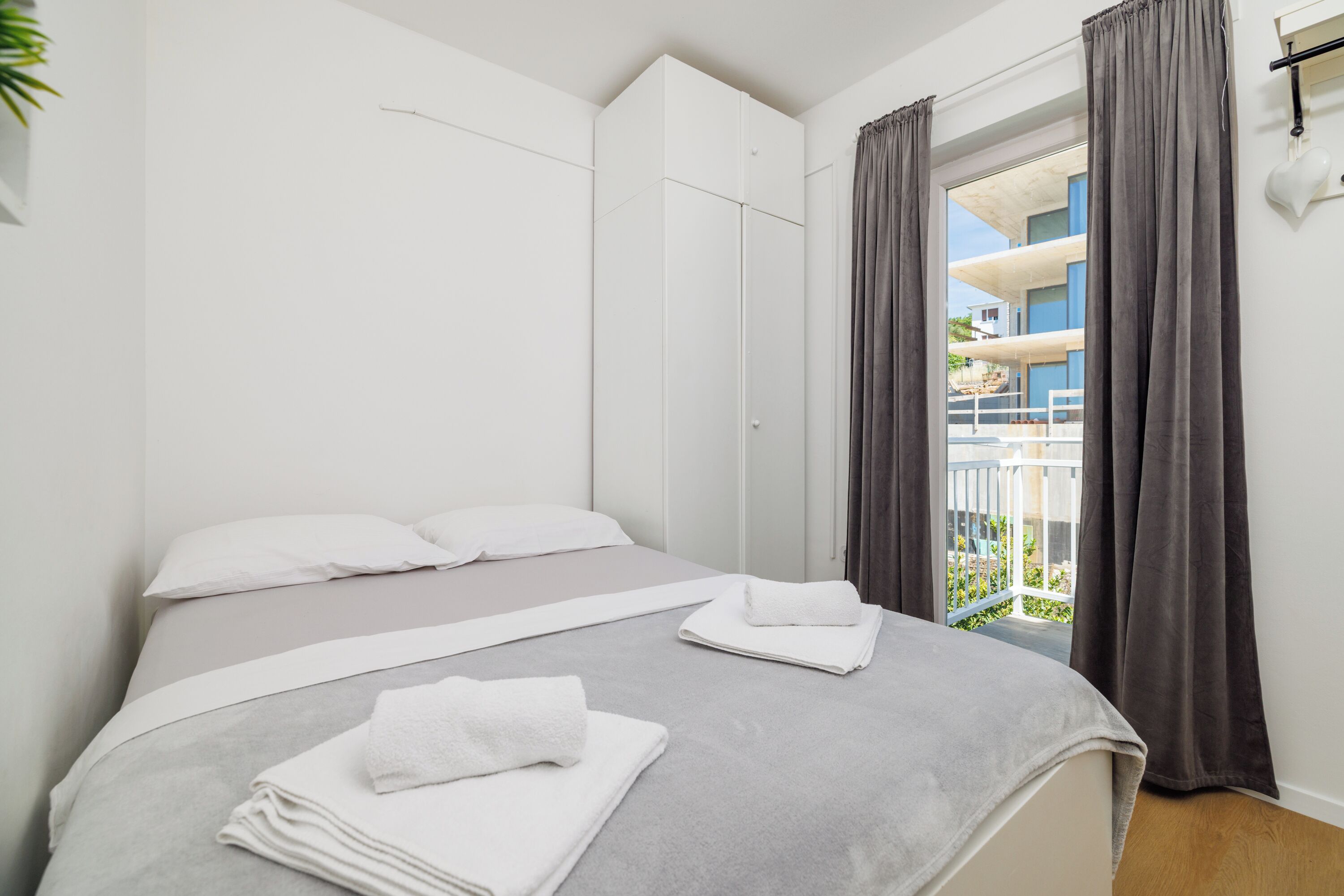 Quarto com cama, cortinas brancas, vista para varanda e guarda-roupa branco.