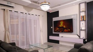Una sala de estar moderna con televisor, sofá, mesa de centro de vidrio y una araña.