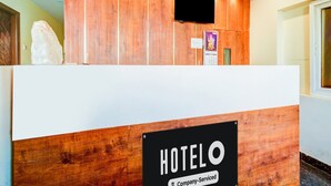 Ein Hotelrezeptionstresen mit Holzausstattung, ein firmenspezifisches Schild, eine Überwachungskamera und ein Fernseher, der über dem Tresen angebracht ist.