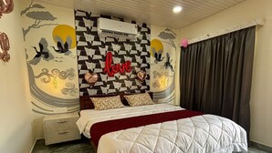 A bedroom with a bed, a wall-mounted air conditioner, a decorative wall with a 'love' sign, and a curtain. - Eleven Eleven Villa (Auroville)
