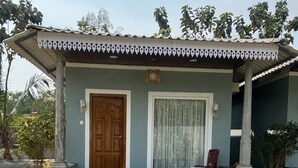 A single-story building with a wooden door, a window with curtains, and a small porch area. - Eleven Eleven Villa (Auroville)