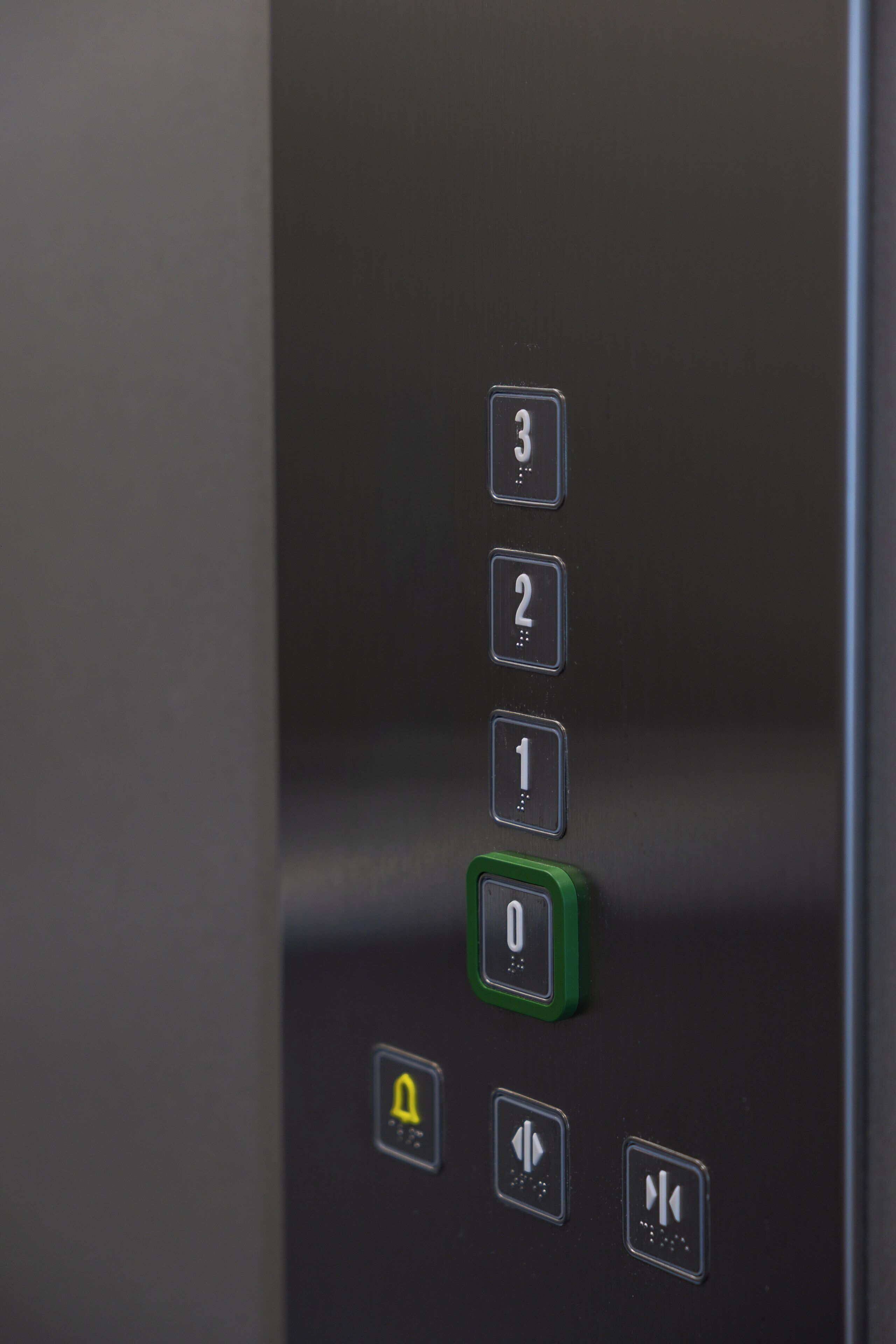 Primer plano de un panel de control de ascensor con botones numerados del 0 al 3, un botón verde y flechas direccionales.