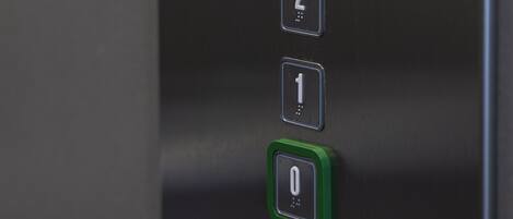 Primer plano de un panel de control de ascensor con botones numerados del 0 al 3, un botón verde y flechas direccionales.
