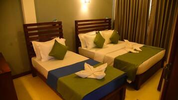 A hotel room with two single beds, each with a wooden headboard, white bedding, and green pillows. There is a small table between the beds, and a light fixture above the headboard.