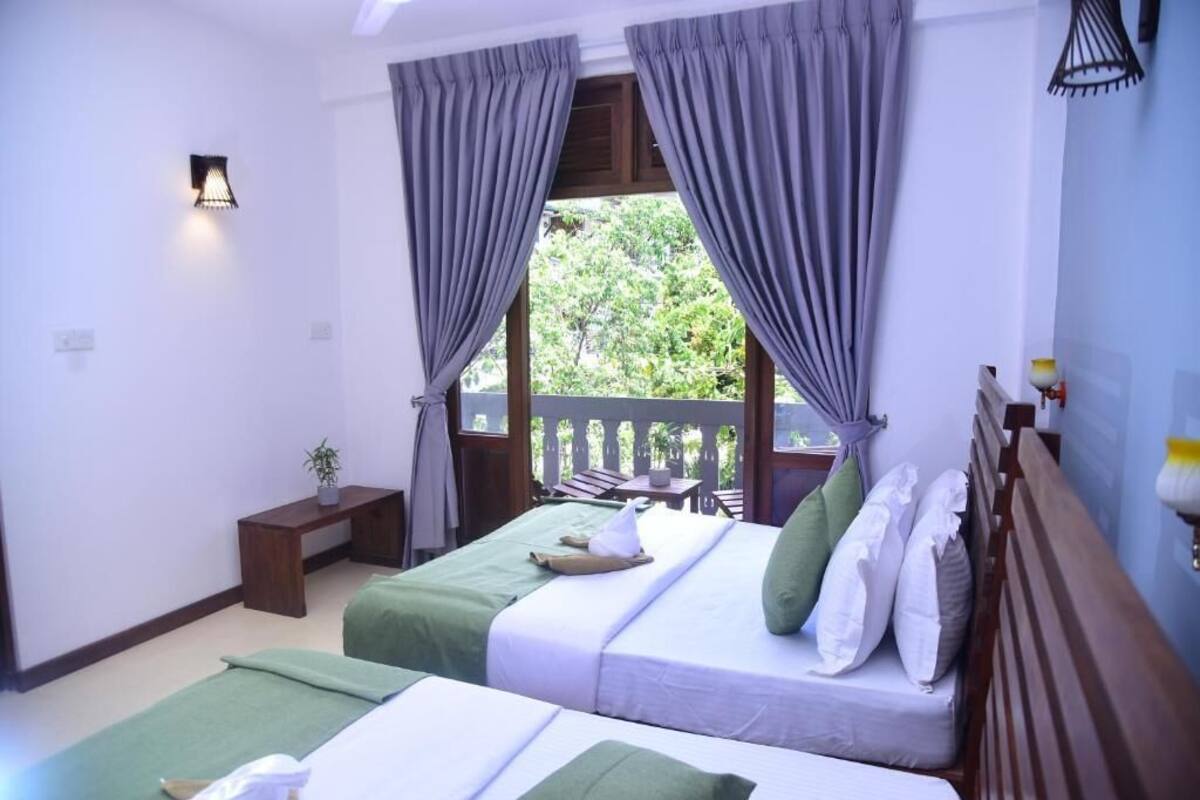 Habitación de hotel con dos camas, una mesita, un banco y un balcón con vistas.