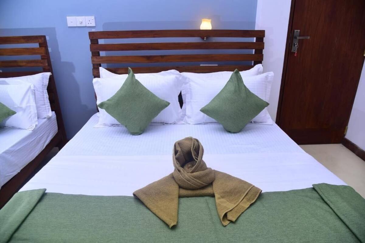 Habitación de hotel con dos camas individuales, cada una con cabecero de madera, ropa blanca y almohadas verdes. Una toalla doblada está sobre la cama.