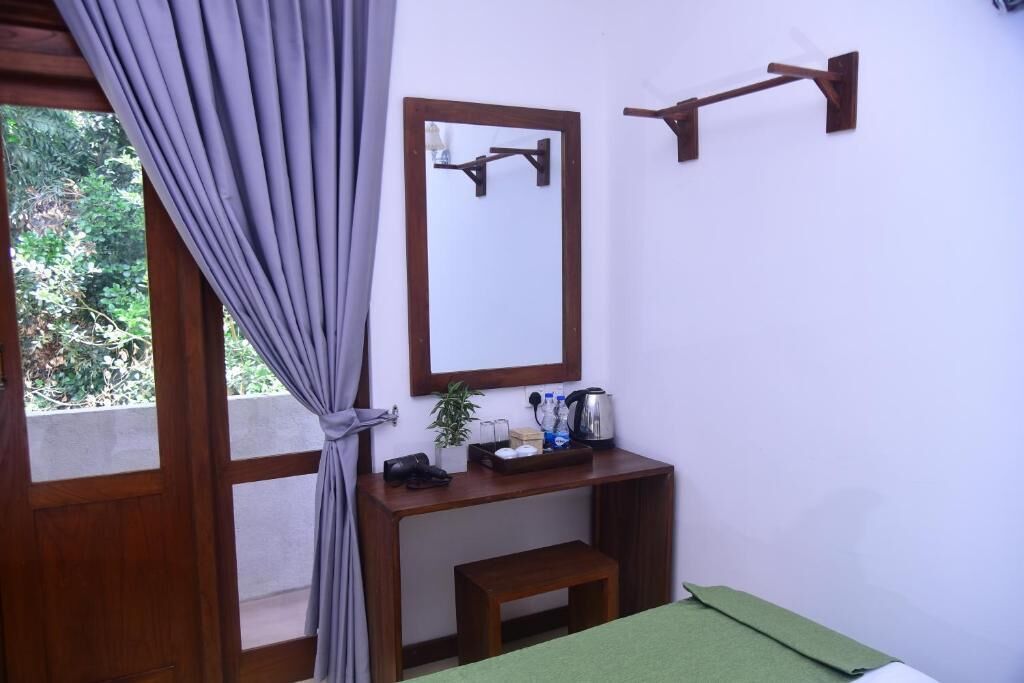 Una habitación con un escritorio de madera, un espejo, un pequeño banco y una colcha verde.