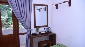 Una habitación con un escritorio de madera, un espejo, un pequeño banco y una colcha verde.