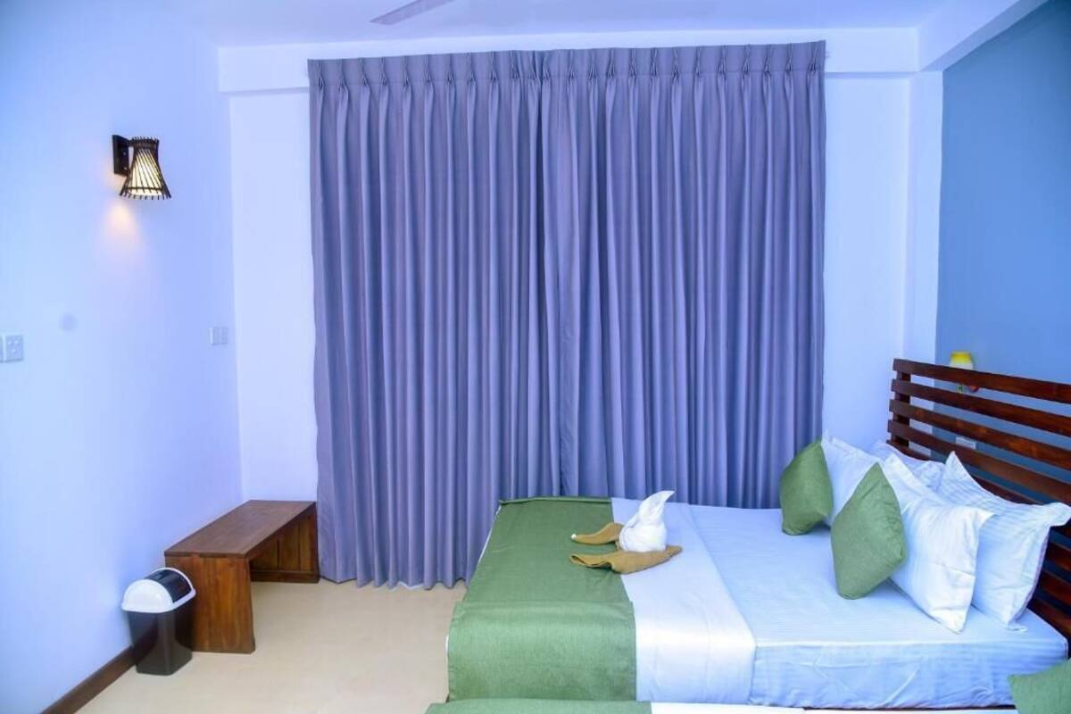 Un dormitorio con cama, almohadas, un banco, una lámpara de pared y una cortina.