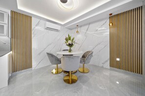 A modern dining area with a marble floor, a round table, and two chairs with gold legs. - Gloucester Place (London)