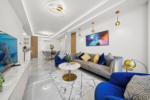A modern living room with a marble floor, a round coffee table, a sofa with blue and gold cushions, a television, and a painting on the wall. - Gloucester Place (London)