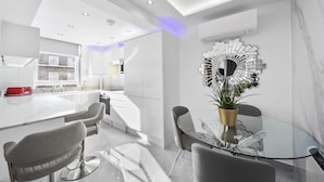 A modern kitchen with white cabinets, a red appliance, and a glass dining table with chairs. - Gloucester Place (London)