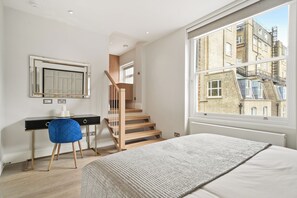 A bedroom with a bed, a desk, a chair, a window, and a staircase. - Gloucester Place (London)