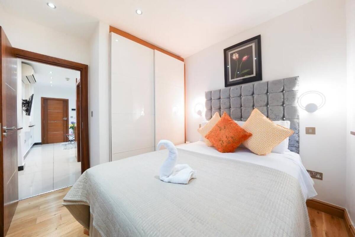 A hotel room with a bed, a headboard, a framed picture, and a swan-shaped towel.