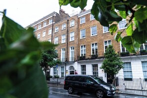 A black van parked on a wet street in front of a row of brick townhouses with white windows and a black metal fence. - Gloucester Place (London)