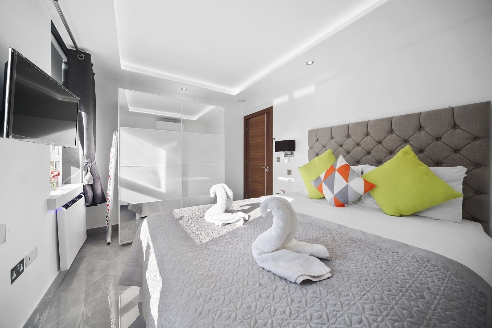 Una habitación de hotel moderna con una cama grande, un televisor de pantalla plana, un armario y un baño.