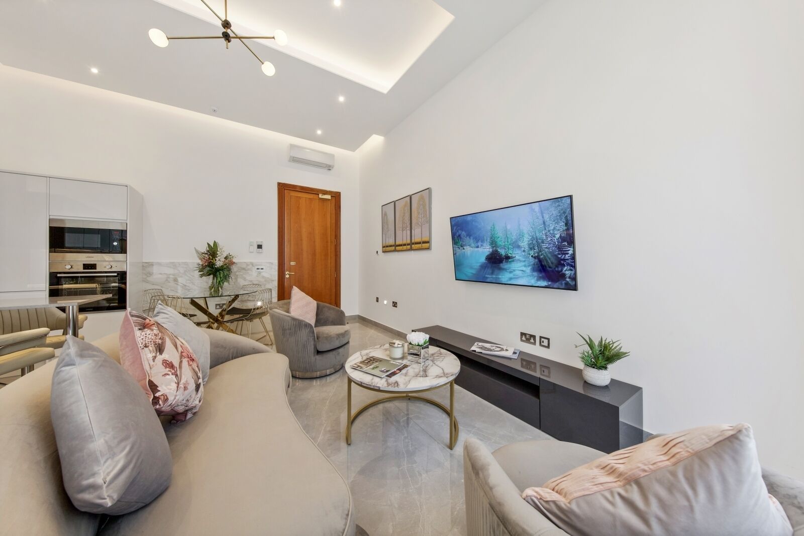 A modern living room with a sofa, armchairs, a coffee table, a TV, and a kitchen area with an oven.