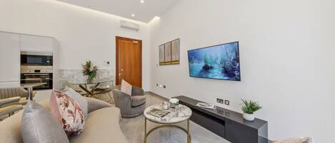 A modern living room with a sofa, armchairs, a coffee table, a TV, and a kitchen area with an oven.