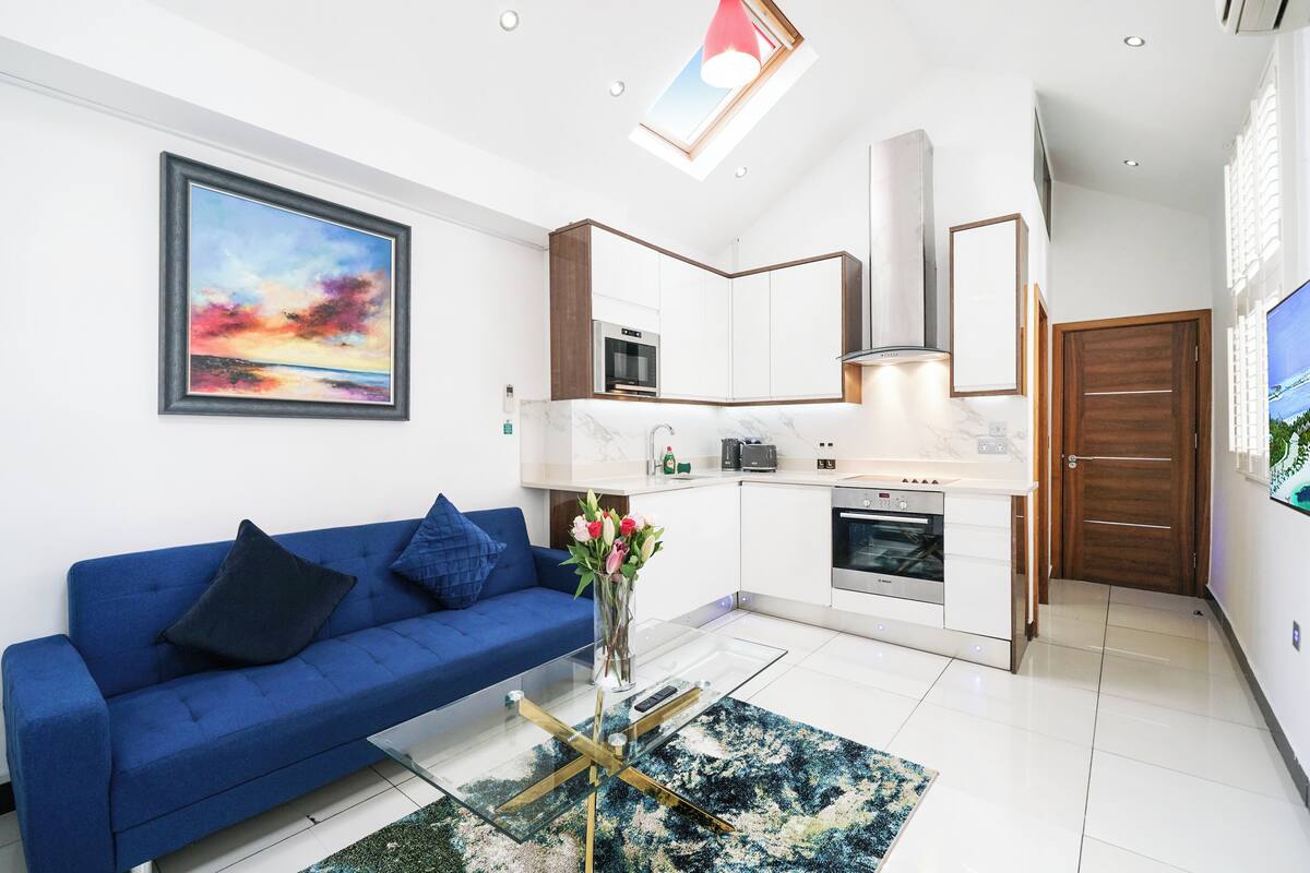 A modern living room with a blue sofa, a glass coffee table, and a painting on the wall.