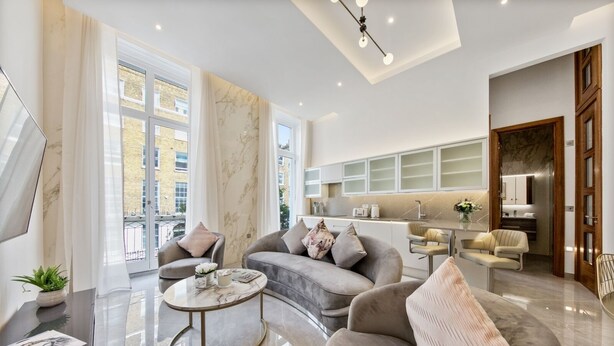 A modern living room with a sofa, armchairs, a coffee table, and a kitchen area with cabinets and a countertop. - Gloucester Place (London)